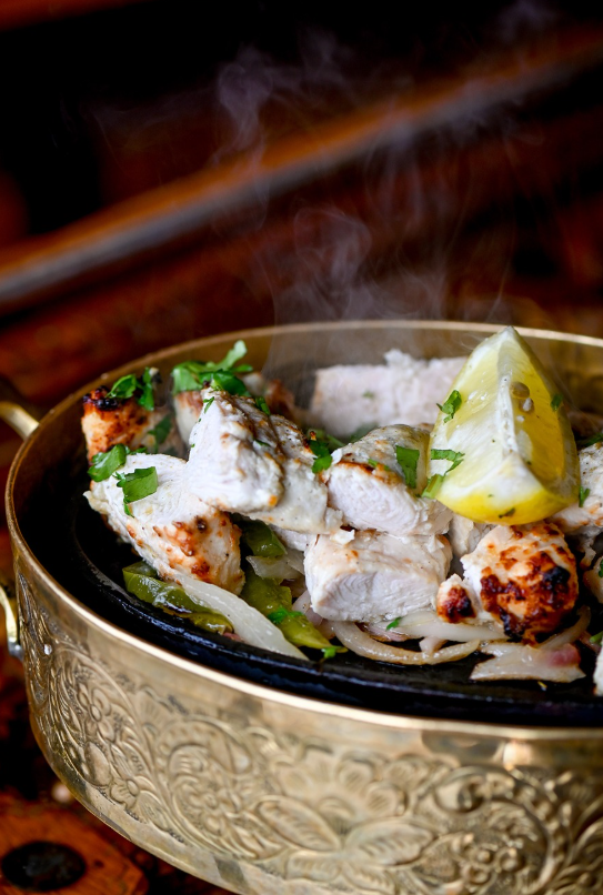 Steaming chicken tikka in an engraved brass skillet with lemon